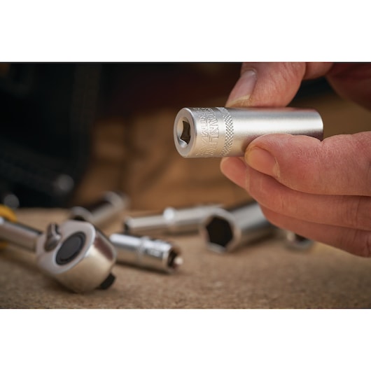 STANLEY FMMT17249-0 socket held in hand, with other sockets and a ratchet on a work surface, close-up.