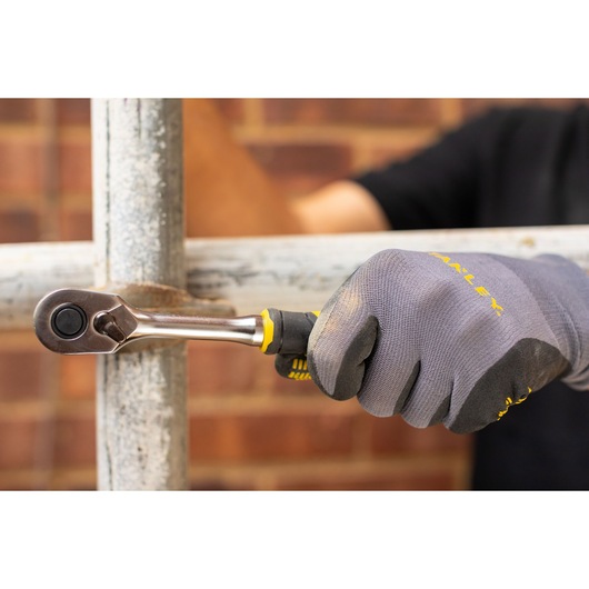 STANLEY FMMT82677-0 ratchet wrench used on metal pipe, close-up, gloved hand holding handle.