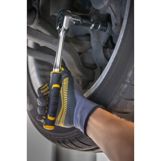 STANLEY FMMT82681-0 ratchet wrench used on car wheel, close-up of gloved hand gripping tool.