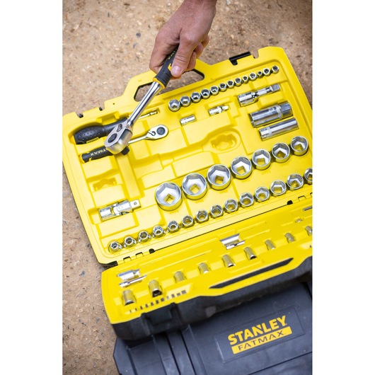 STANLEY FMMT82827-1 socket and ratchet set in yellow and black case, with hand holding ratchet, outdoor setting.
