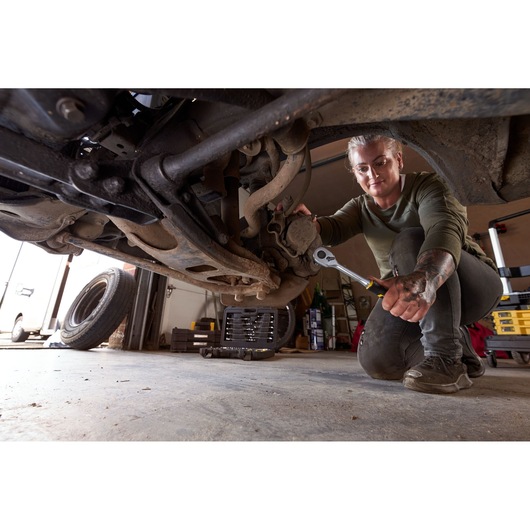 STANLEY FMMT82827-1 socket and wrench set in use under a car in a garage, mechanic working on suspension.