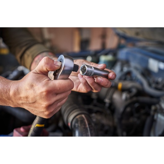 Photo of STANLEY FATMAX FMMT82827-1 ratchet and socket from the 50-piece wrench set held by hands near a car engine.