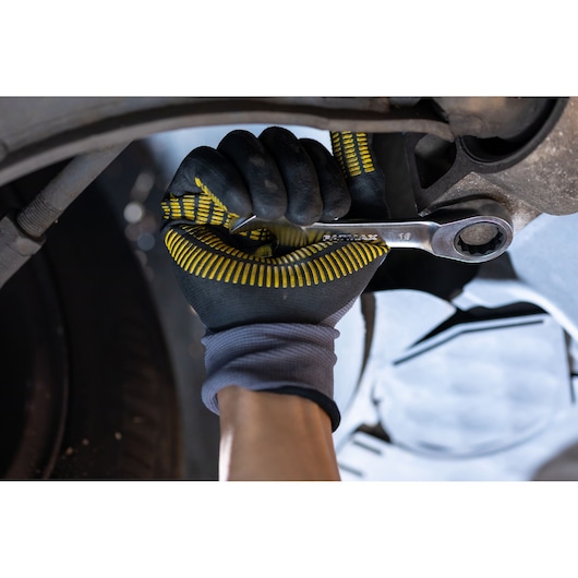 STANLEY FMMT82900-0 ratcheting wrench held by gloved hand under vehicle, close-up, automotive tool.