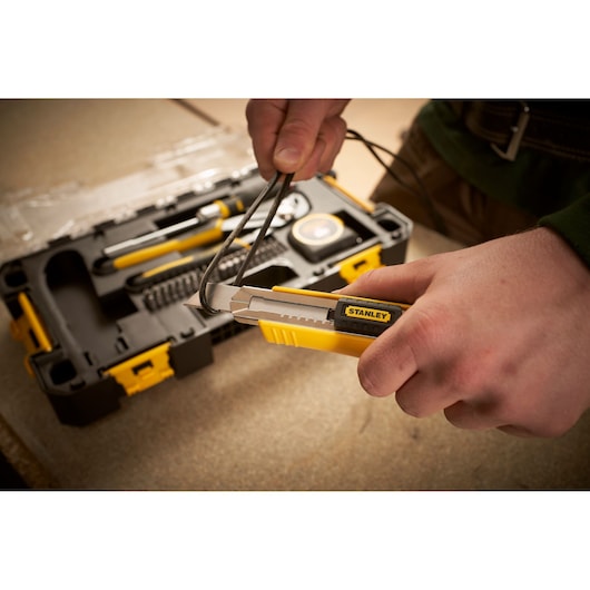 STANLEY FMMT98106-1 utility knife cutting black cable, toolkit in background, angled view.