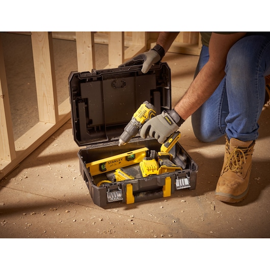 STANLEY FMST1-71967 toolbox with yellow and black hand tools on construction site floor, lid open.