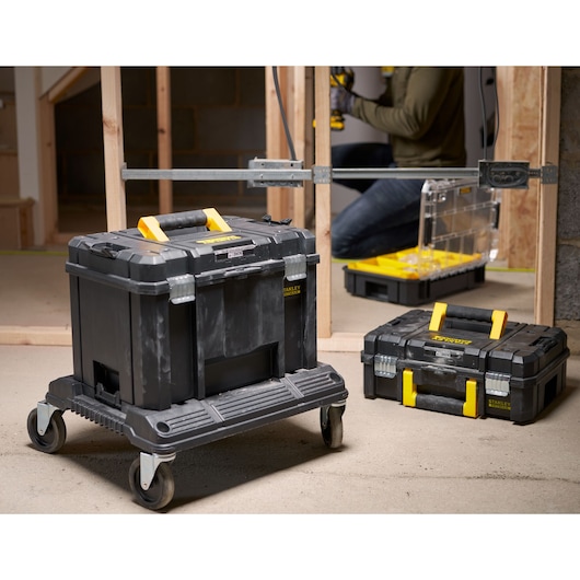 STANLEY FMST1-71971 toolbox on wheeled base, black with yellow handle, in workshop setting.
