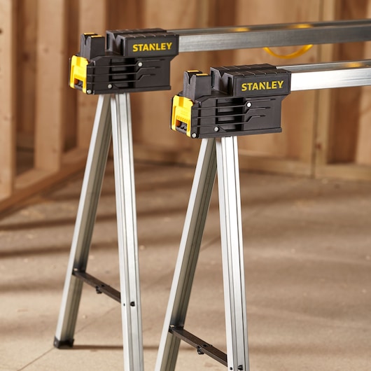 STANLEY FMST1-75763 folding metal saw horses with yellow and black clamps, shown in workshop setting.
