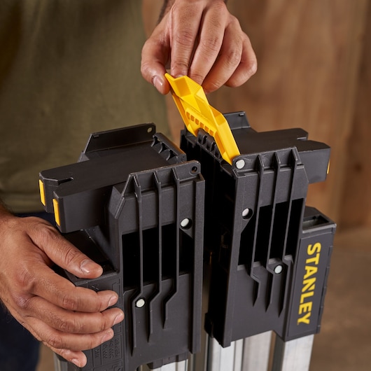 Photo of STANLEY FMST1-75763 sawhorse in black and yellow being adjusted by hand, close-up view.