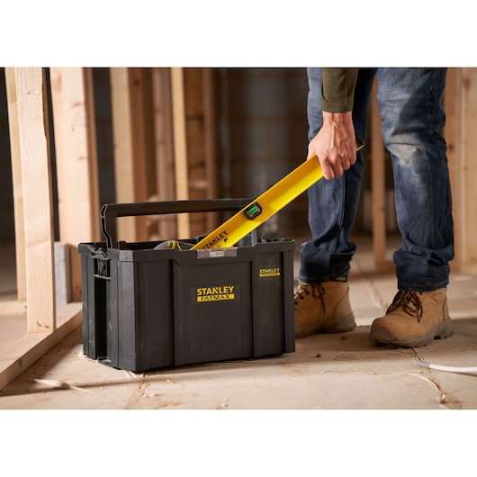 Stanley FMST1-75794 toolbox with handle, shown on construction site, person placing yellow level inside