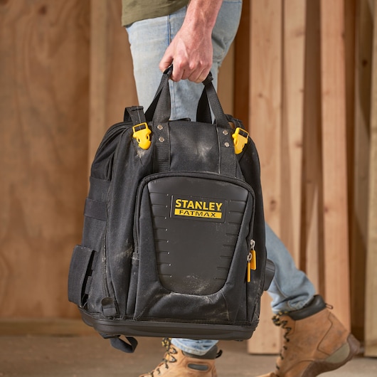 STANLEY FMST1-80144 tool backpack with hard front panel and yellow accents, shown being carried by hand.