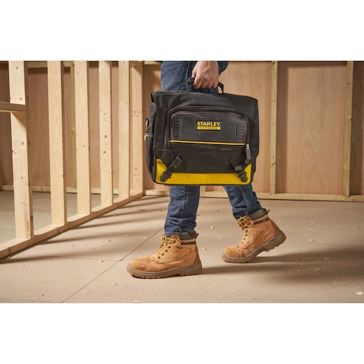 STANLEY FMST1-80149 tool bag carried by person wearing work boots in unfinished construction area.