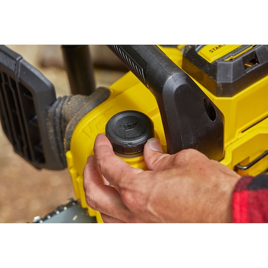 STANLEY SFMCCS630B chainsaw close-up with hand adjusting oil cap, yellow and black design.