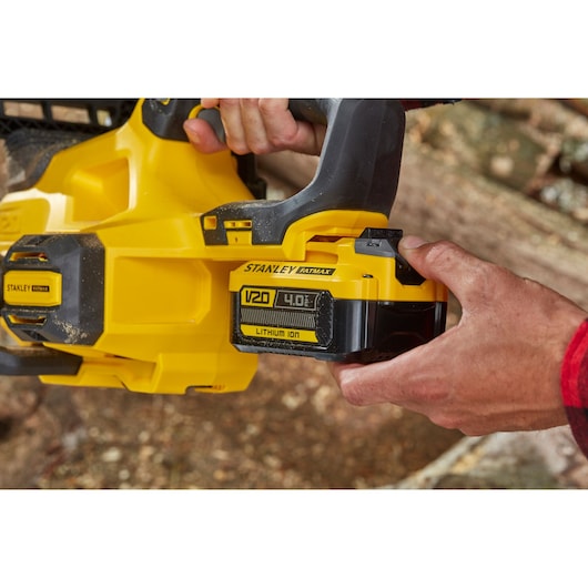 Photo of STANLEY SFMCCS630M1 V20 Fatmax chainsaw with 4.0 Ah lithium-ion battery being inserted outdoors.