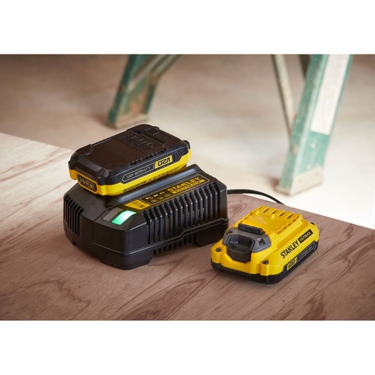 STANLEY SFMCD700C2K battery charger with two yellow-black lithium-ion batteries on a wooden surface.