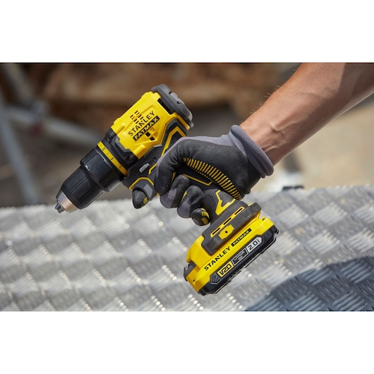 Photo of STANLEY SFMCD710D2K cordless drill in use, yellow and black design, battery visible, held by gloved hand.