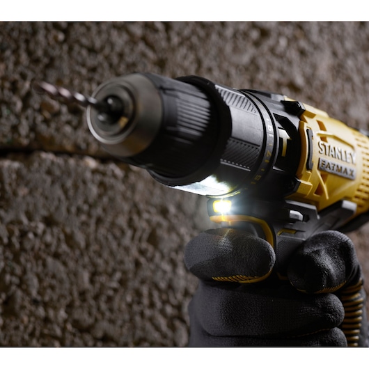 STANLEY SFMCD711C2K drill with LED light, close-up view, drilling into textured wall, gloved hand holding tool.