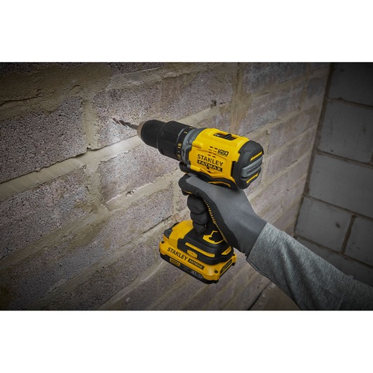 Photo of STANLEY SFMCD715C2K drill in use against a brick wall, yellow and black cordless power tool.