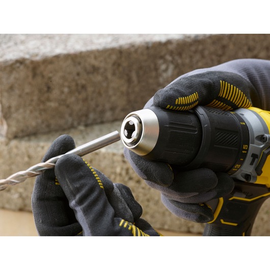 STANLEY SFMCD715C2K cordless drill held in gloved hands, inserting a metal drill bit, close-up view.