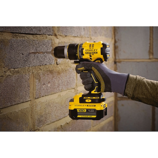 STANLEY SFMCD721M2K cordless drill in use, drilling into brick wall, yellow and black design, Photography product.