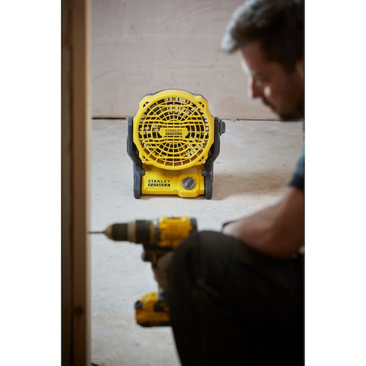 Photo of STANLEY SFMCE001B yellow portable fan on floor with construction tool in foreground.