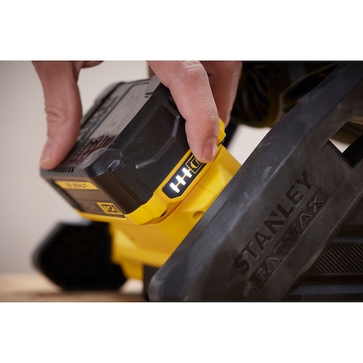 Close-up of a hand inserting battery into STANLEY SFMCE001B power tool, showing yellow and black details.