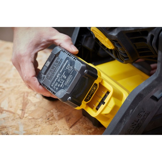 Photo of STANLEY SFMCE001B battery being inserted into a yellow power tool on a wood surface.