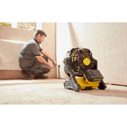 Photo of STANLEY SFMCE001B portable cordless fan in a room with a worker near the wall.