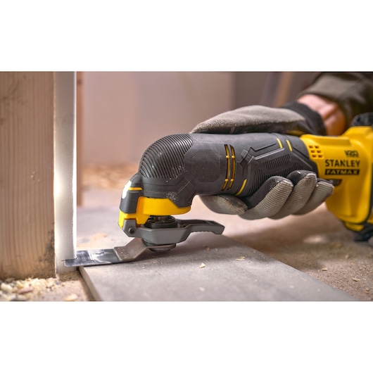 Photo of STANLEY SFMCE500B multitool cutting wood, gloved hand holding black and yellow tool.