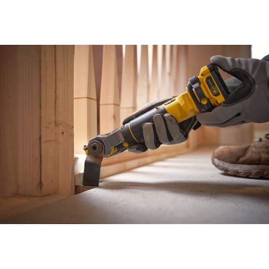 STANLEY SFMCE500B oscillating multi-tool in use on wood flooring, handheld by gloved worker.