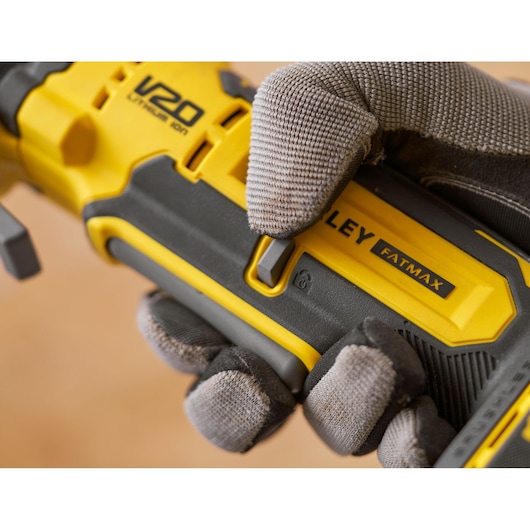 Photo of STANLEY SFMCE510B FATMAX power tool handle, V20 branding, gloved hand pressing switch, close-up.