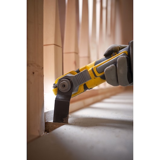 STANLEY SFMCE510B oscillating tool cutting wood near baseboard, close-up in construction setting.