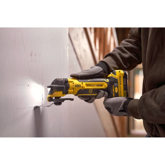 Stanley SFMCE510B oscillating tool cutting drywall, close-up in use with gloved hands.