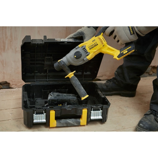 STANLEY SFMCH900B rotary hammer being placed in a black and yellow carrying case on a workshop floor.