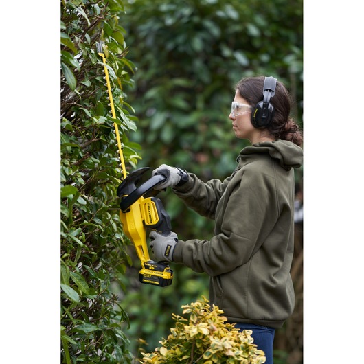 STANLEY SFMCHT855B hedge trimmer in use outdoors, yellow and black, battery-powered, garden scene.