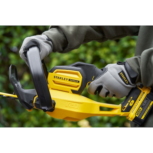 Photo of STANLEY SFMCHT855B cordless hedge trimmer in use, yellow and black design, gloved hands holding handle.