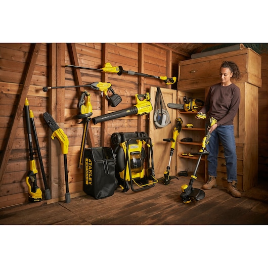 STANLEY SFMCHT855B cordless garden tools and accessories displayed in wooden shed, photo of person holding trimmer.