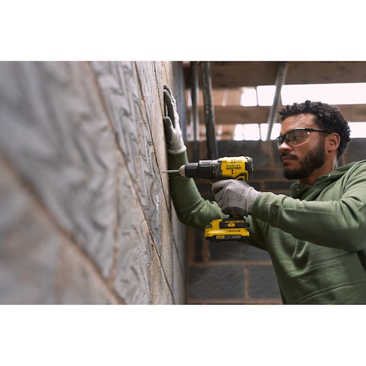 Photo of STANLEY SFMCK461D2T cordless drill in use drilling into a block wall, construction setting.