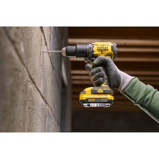 Stanley SFMCK461D2T cordless drill in use, drilling concrete wall, yellow and black, close-up side view.