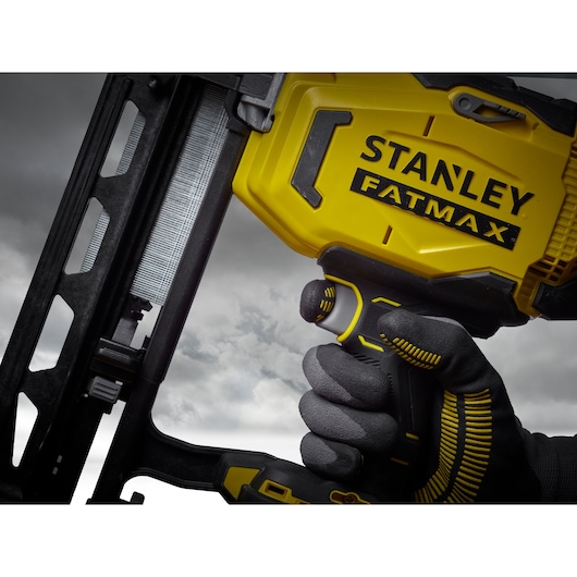 Photo of STANLEY SFMCN616D2K cordless nailer, close-up angled view, yellow and black design, gloved hand holding.