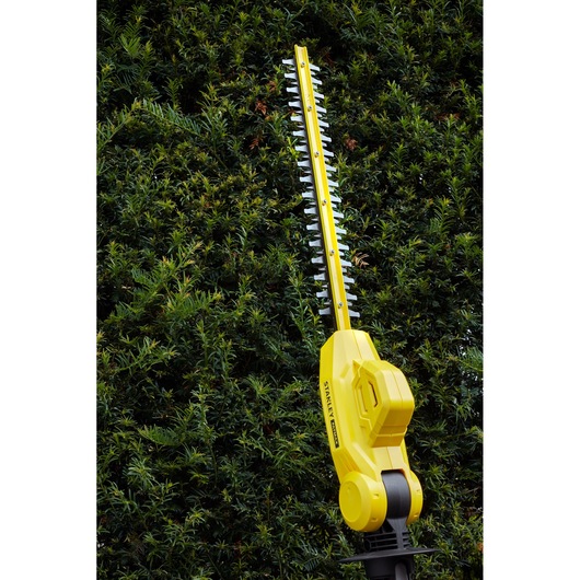 STANLEY SFMCPH845M1 hedge trimmer in use, yellow body with black accents, trimming green hedge.