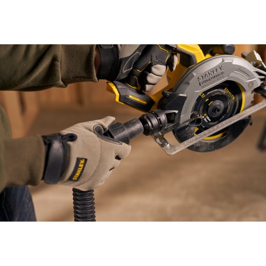STANLEY SFMCS550B circular saw with vacuum attachment held by gloved hands in workshop setting.
