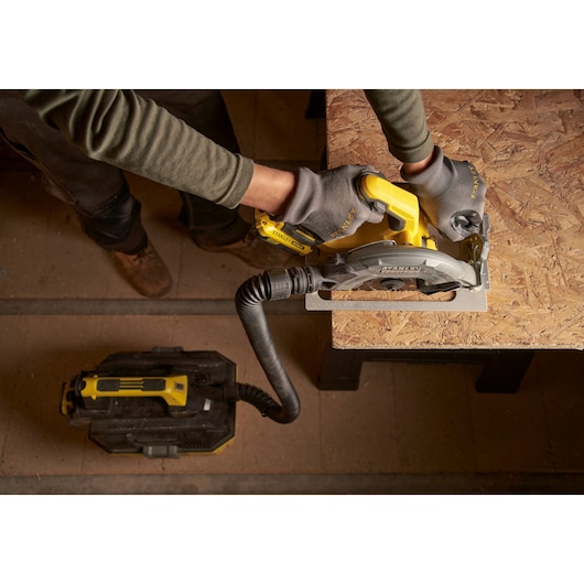 STANLEY SFMCS550M2K circular saw with dust extraction in use on wood panel, top view photography.