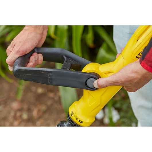 Close-up of STANLEY SFMCST933B string trimmer handle being adjusted, yellow and black details, outdoor setting.