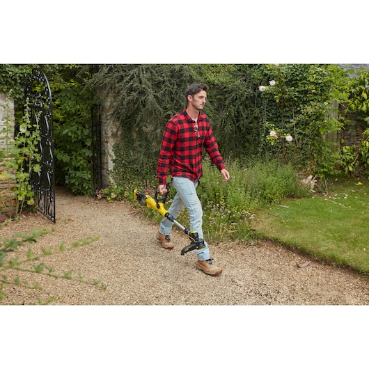 STANLEY SFMCST933B string trimmer held by a person outdoors on a garden path.