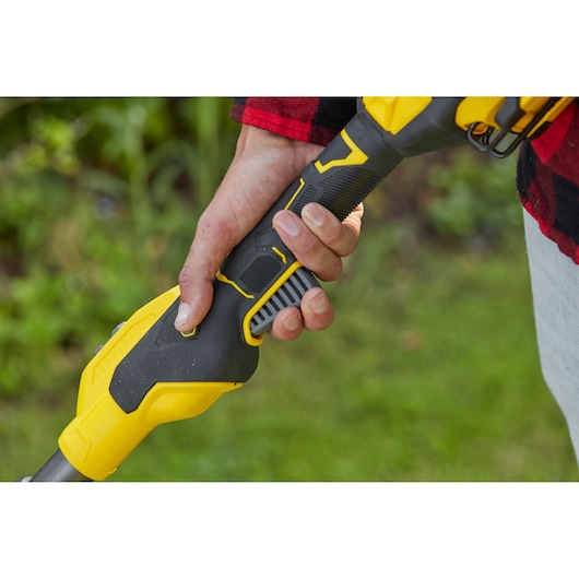 Close-up photo of a hand holding the STANLEY SFMCSTB933B grass trimmer handle, black and yellow design, outdoor use.