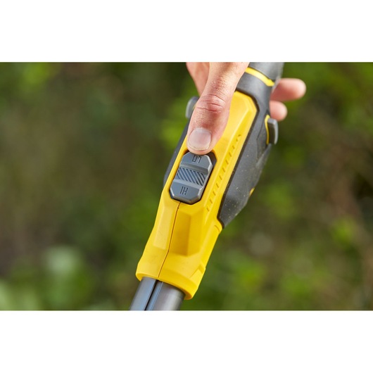 STANLEY SFMCSTB933B trimmer close-up of yellow and black handle with speed switch and thumb operation outdoors.