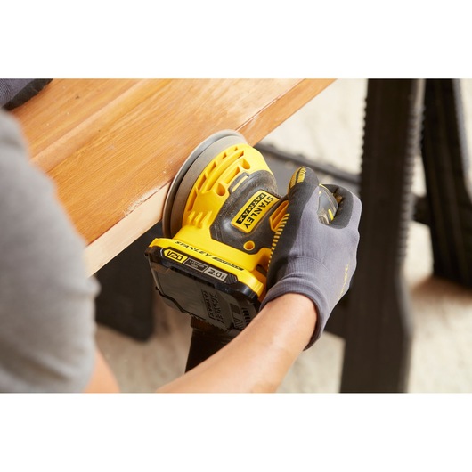 Photo of STANLEY SFMCW220B cordless sander in use on wooden surface, close-up angle.