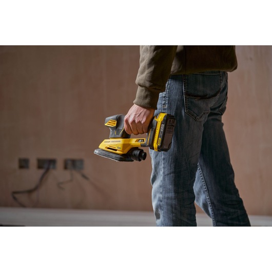 Photo of STANLEY SFMCW221B cordless sander held by a person in a workwear setting.
