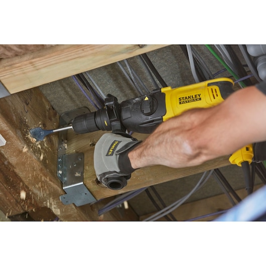 STANLEY SFMEH210K hammer drill in use drilling wood beam, close-up angle, worker wearing STANLEY gloves.