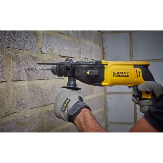 STANLEY SFMEH210K rotary hammer drill in use against a brick wall, close-up view, user wearing Stanley gloves.